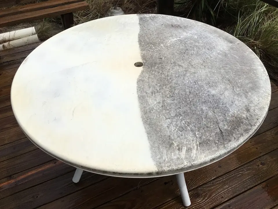 Outdoor patio table half cleaned: bright white on one side, gray mildew on the other